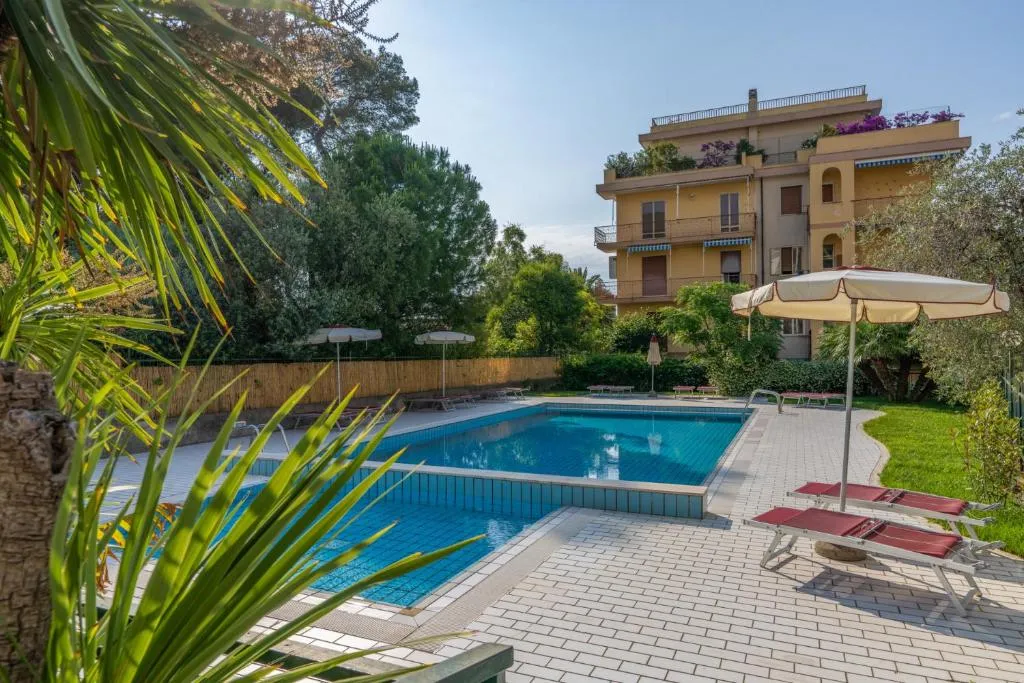 Piscina circondata da pavimentazione, lettini e giardino con palme accanto all'edificio