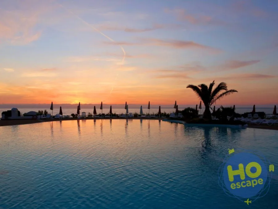 Piscina a sfioro con vista mare al tramonto, ombrelloni chiusi e palma in silhouette