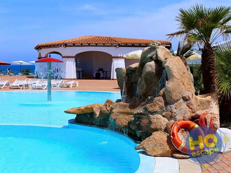 Piscina con cascata su roccia artificiale e giochi d'acqua, vista mare e palme