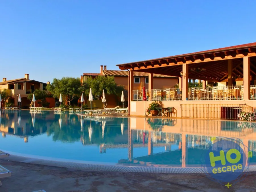 Piscina del resort al tramonto con riflessi sull'acqua e ristorante coperto adiacente