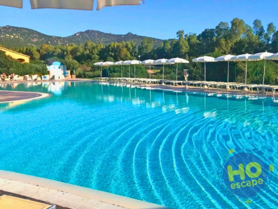 Piscina dalle acque azzurre cristalline con lettini e ombrelloni e vegetazione circostante