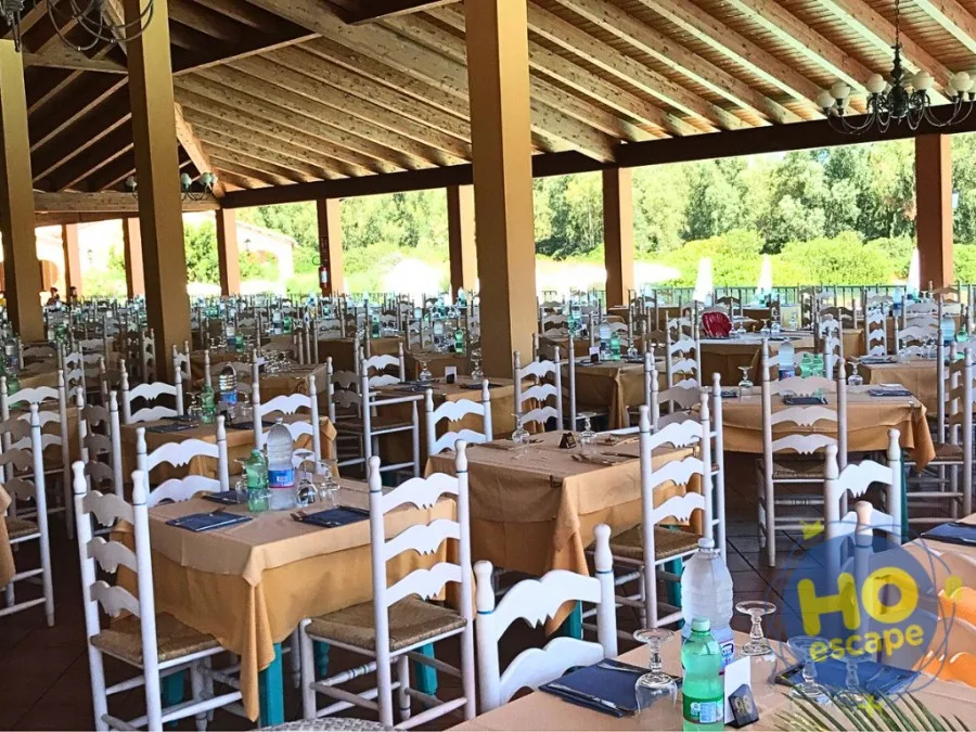 Ristorante coperto all'aperto con tavoli apparecchiati con tovaglie beige e sedie bianche in legno