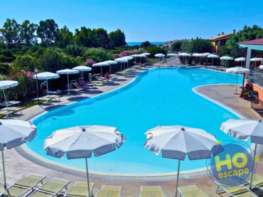 Ampia piscina con ombrelloni bianchi e lettini circondata da verde e fiori
