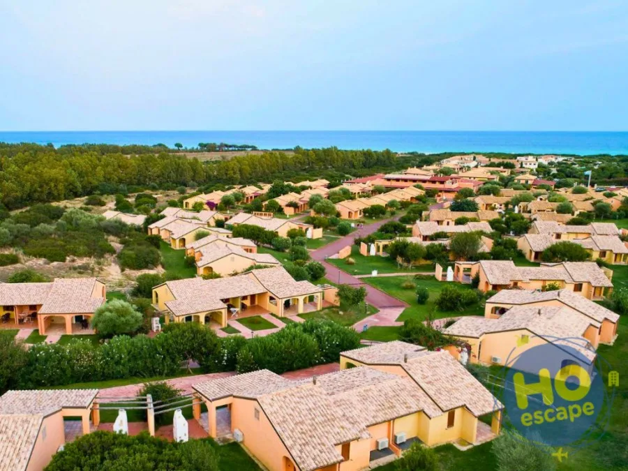 Vista aerea del resort con villette color terracotta immerse nel verde e mare sullo sfondo