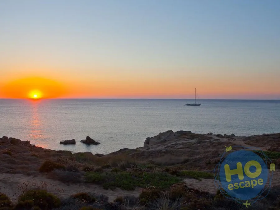Tramonto sul mare con barca a vela e costa rocciosa