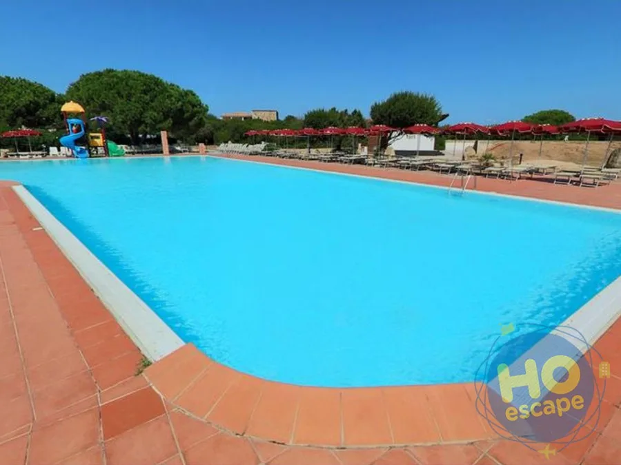 Ampia piscina rettangolare con bordo in cotto, ombrelloni rossi e scivolo per bambini