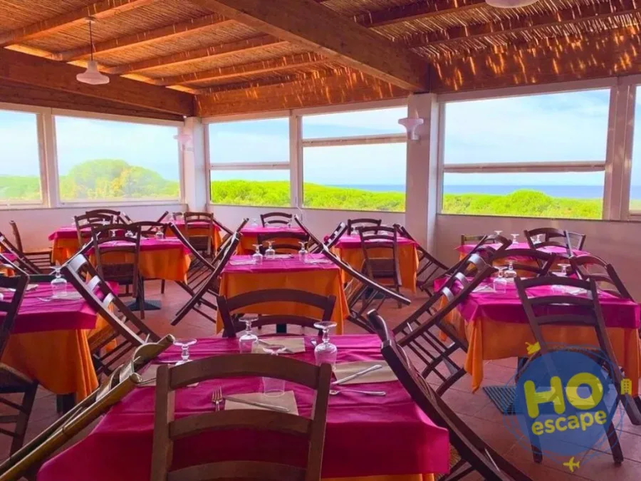 Sala ristorante panoramica con tovaglie rosa e arancio e ampie vetrate sul verde e sul mare
