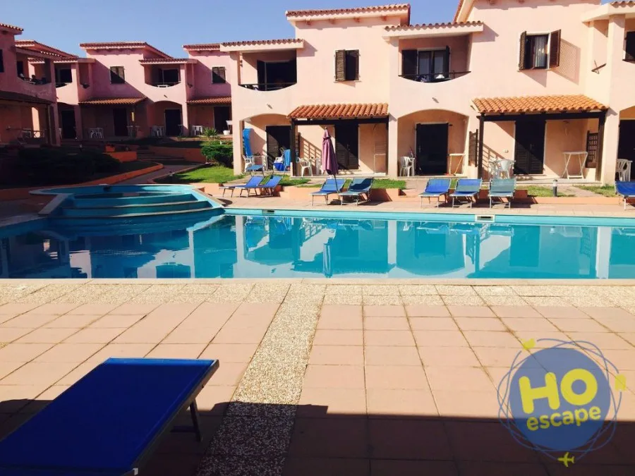 Piscina del residence con lettini blu e villette rosa sullo sfondo