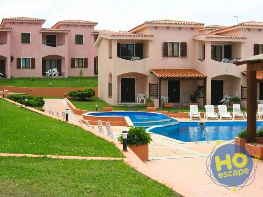 Giardino verde con piscina e villette rosa del residence, prato curato e camminamenti