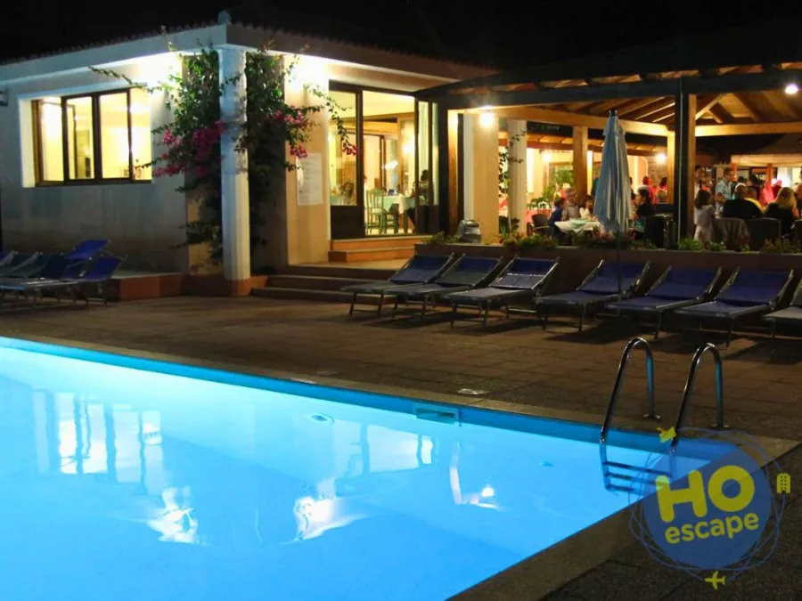 Piscina illuminata di sera con lettini blu e area ristorante con tavoli all'aperto