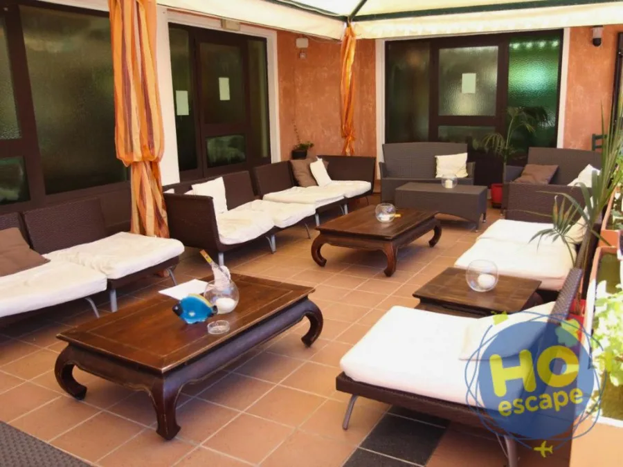 Area lounge coperta con divani in rattan scuro, cuscini bianchi e tavolini bassi in legno