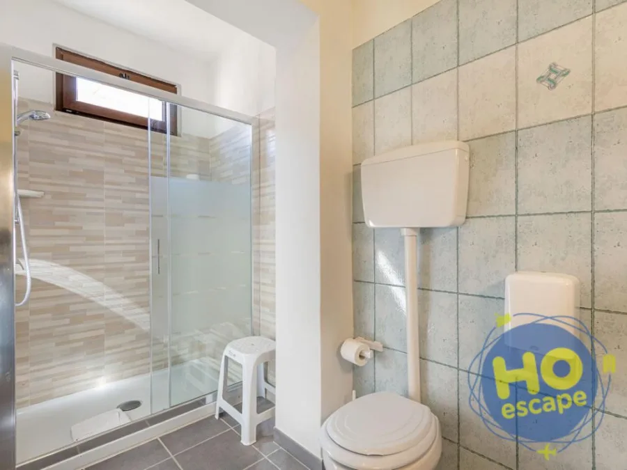Bagno con doccia a vetri, sgabello e sanitari su pareti piastrellate