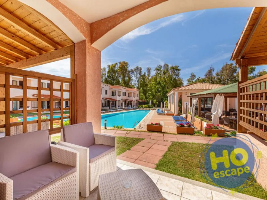 Veranda coperta con poltrone in rattan affacciata sulla piscina circondata da giardino e residenze
