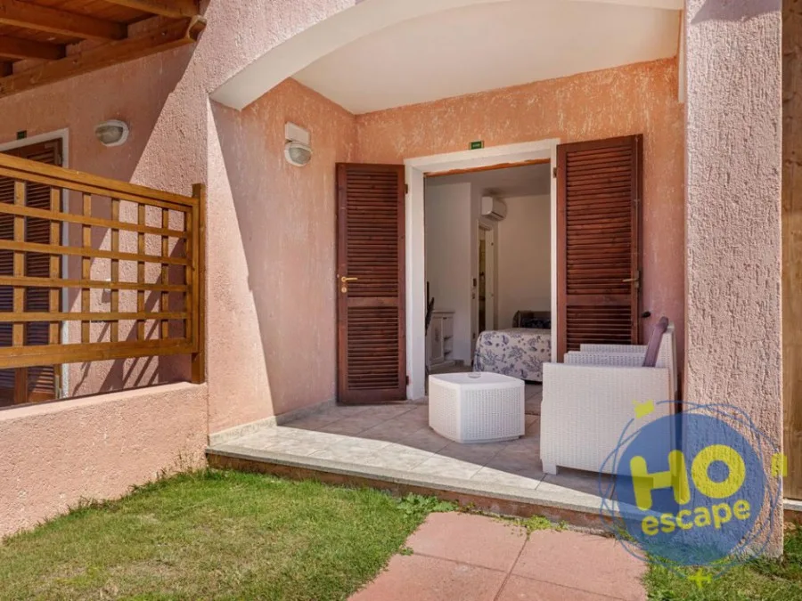 Ingresso esterno di un appartamento con portico, poltrone in rattan e prato verde