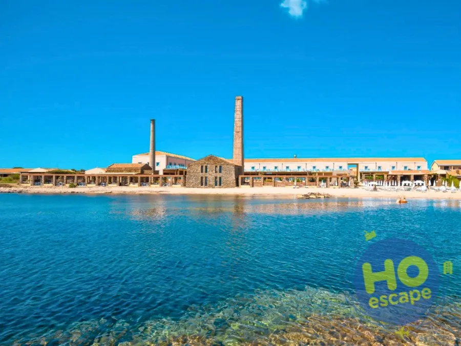 Edificio storico in pietra con ciminiere affacciato sulla spiaggia e mare azzurro