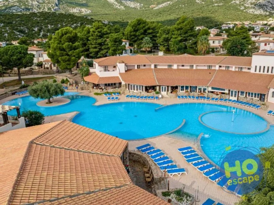 Vista aerea della grande piscina con lettini blu e edifici del resort tra il verde