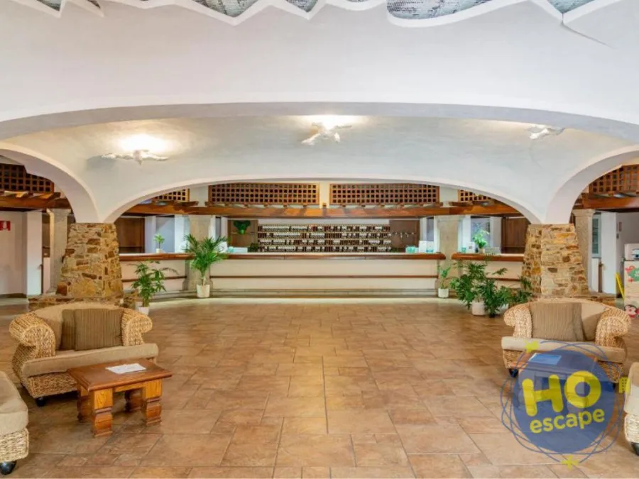 Ampia hall interna con banco reception, archi bianchi e poltrone in vimini