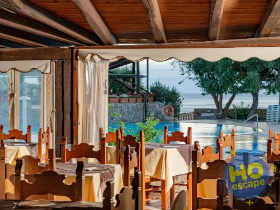 Sala ristorante con tavoli e sedie in legno affacciata sulla piscina e sul mare