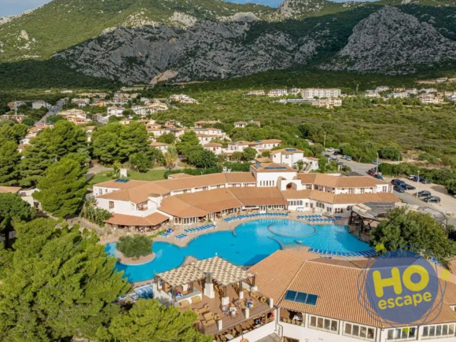 Vista aerea del resort con piscina, edifici e montagne della Sardegna sullo sfondo