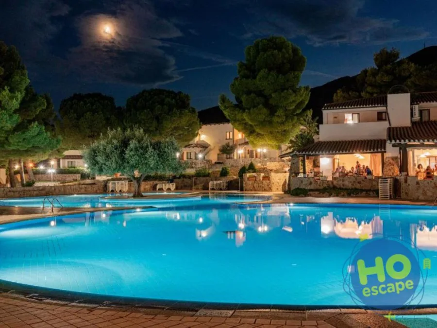 Piscina del resort illuminata di sera con la luna e gli edifici sullo sfondo
