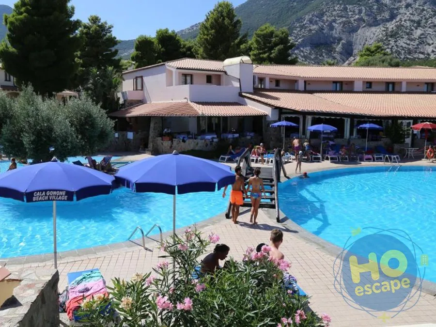 Piscina del Cala Gonone Beach Village con ombrelloni blu, lettini e ospiti, immersa nel verde e tra le montagne