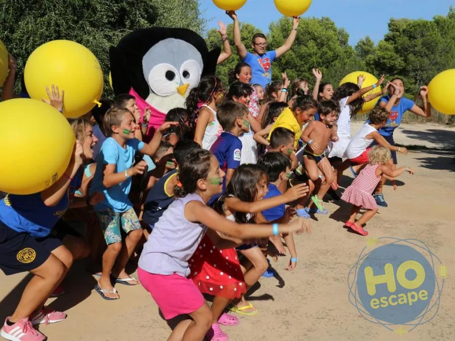 Bambini e animatori con palloni gialli e mascotte pinguino durante un'attività all'aperto