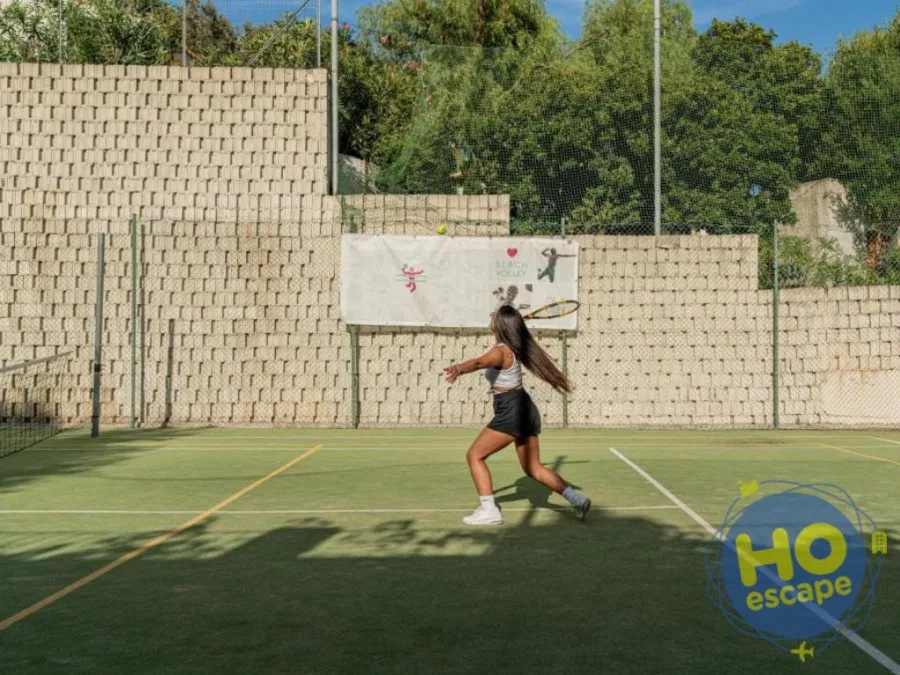 Ragazza gioca a tennis su campo in erba sintetica circondato da muri in pietra