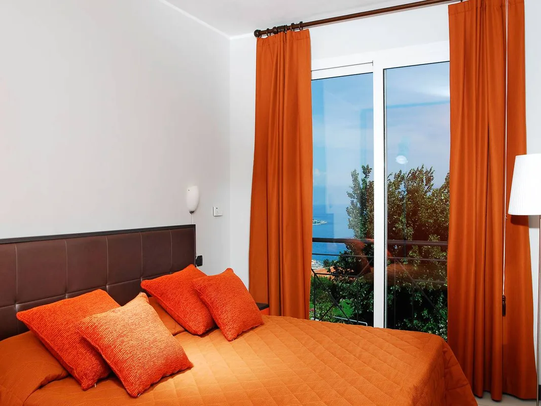 Camera da letto con cuscini arancioni, testiera in pelle e finestra con vista mare