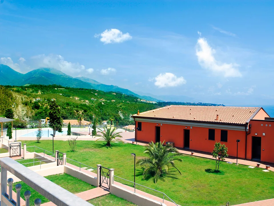 Veduta del residence con piscina, giardino e palme con sfondo di montagne e mare