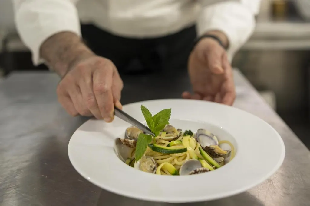 Chef impiatta spaghetti con vongole, zucchine e menta su piatto bianco