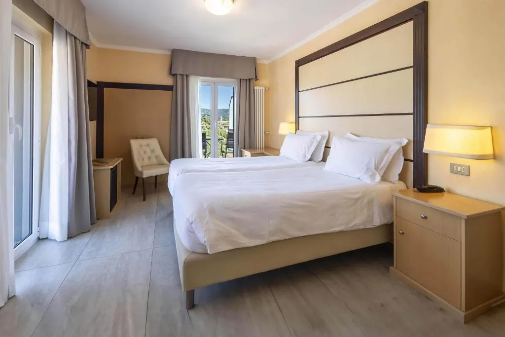 Camera matrimoniale moderna con letto bianco, testiera in legno e finestra con vista sulle colline