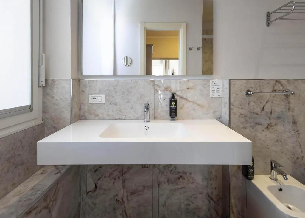 Bagno moderno con lavabo bianco sospeso, specchio e rivestimento in marmo