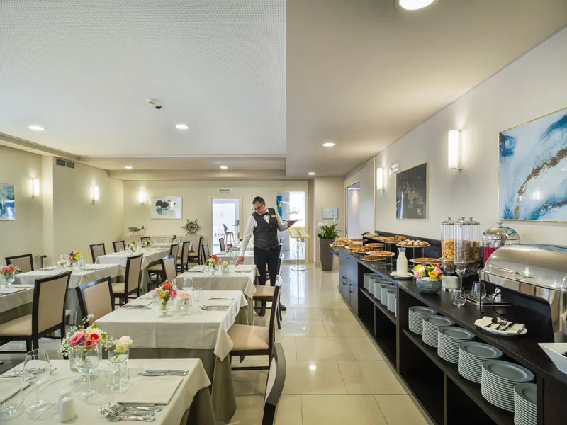 Sala colazione con buffet e tavoli apparecchiati con fiori
