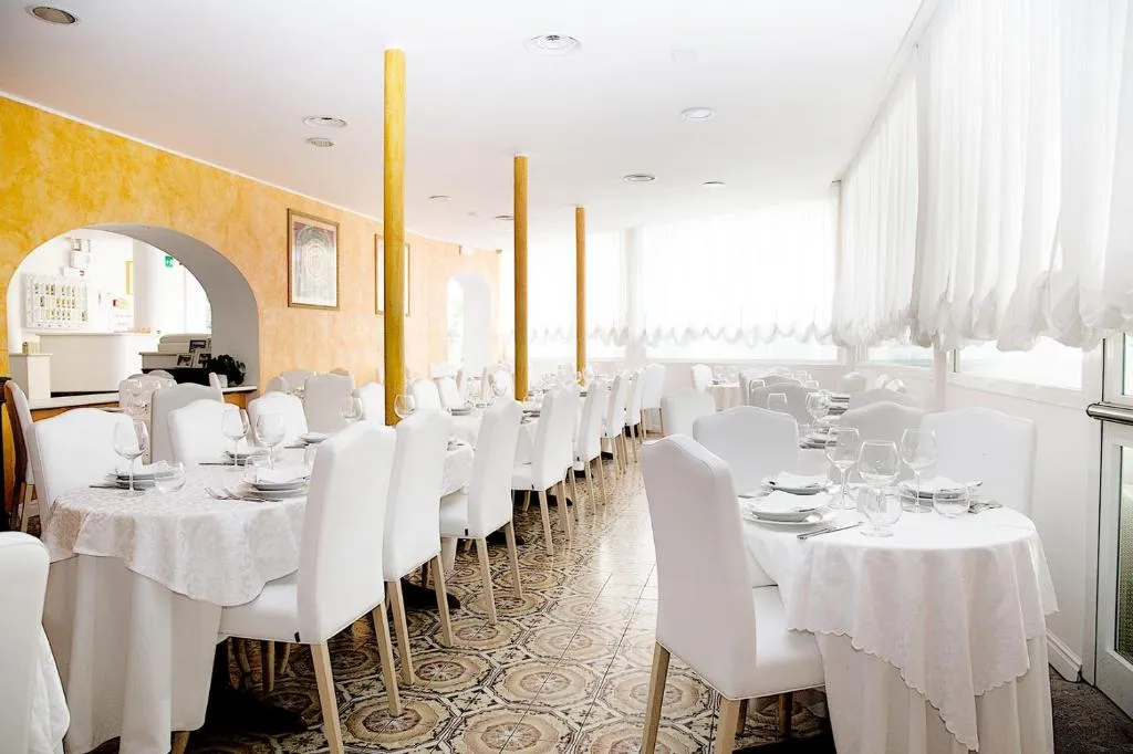 Sala ristorante con tavoli rotondi apparecchiati e sedie bianche