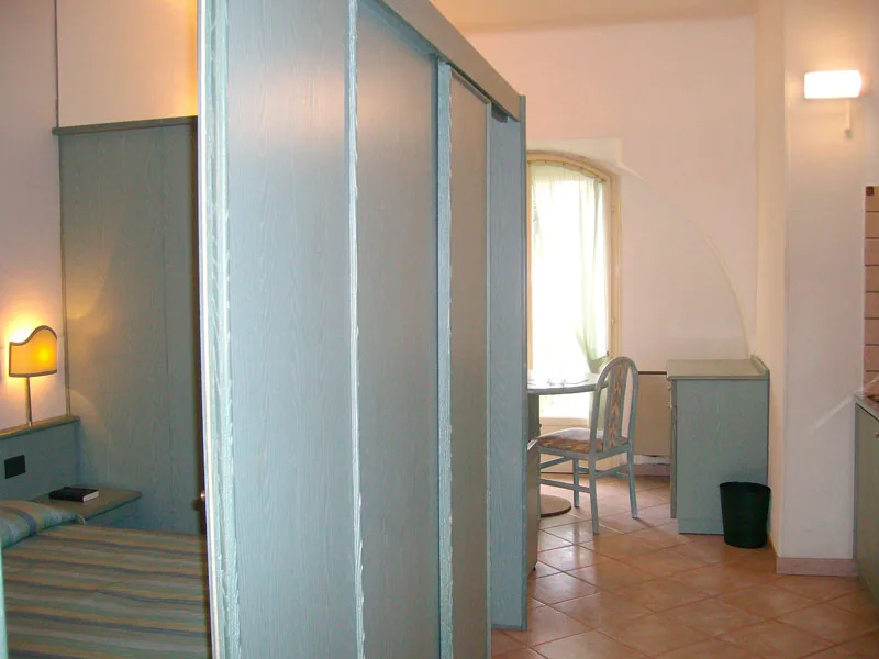 Interno con letto, separé in legno, scrivania e angolo cottura
