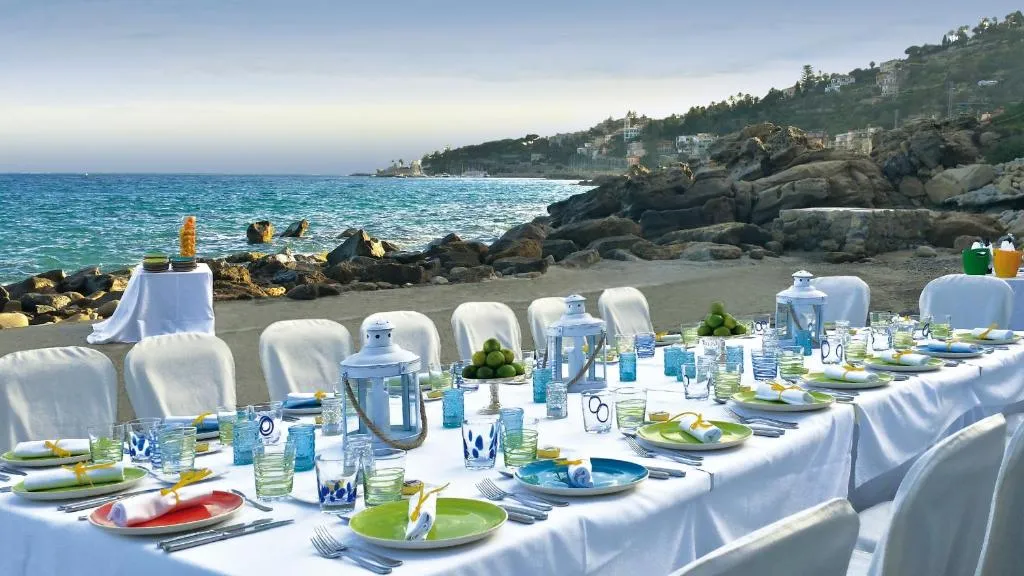 Tavolo apparecchiato per cena sulla spiaggia con stoviglie colorate e vista sul mare