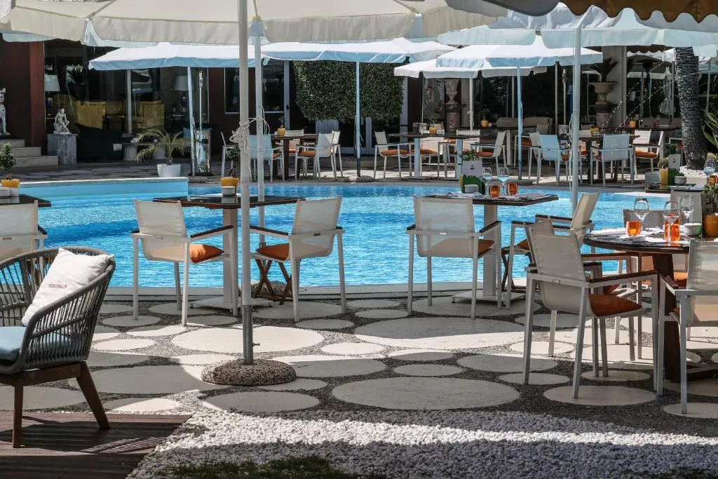 Tavoli del ristorante a bordo piscina con sedie bianche e pavimento decorativo a ciottoli