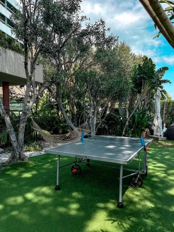 Tavolo da ping pong su prato verde circondato da alberi e amaca