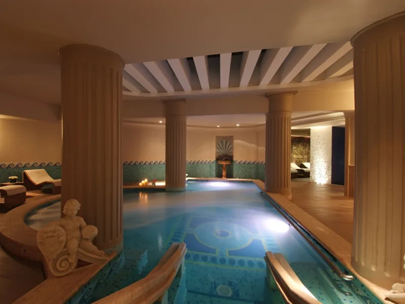 Piscina coperta termale con colonne classiche, illuminazione soffusa e statua decorativa
