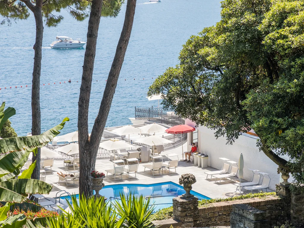 Vista della piscina e del solarium sul mare tra i pini, con barca in navigazione