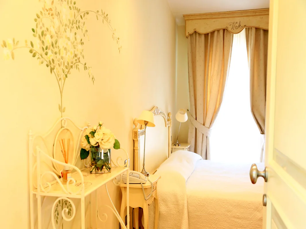 Camera luminosa con decorazione floreale a parete, letto in ferro battuto e fiori freschi
