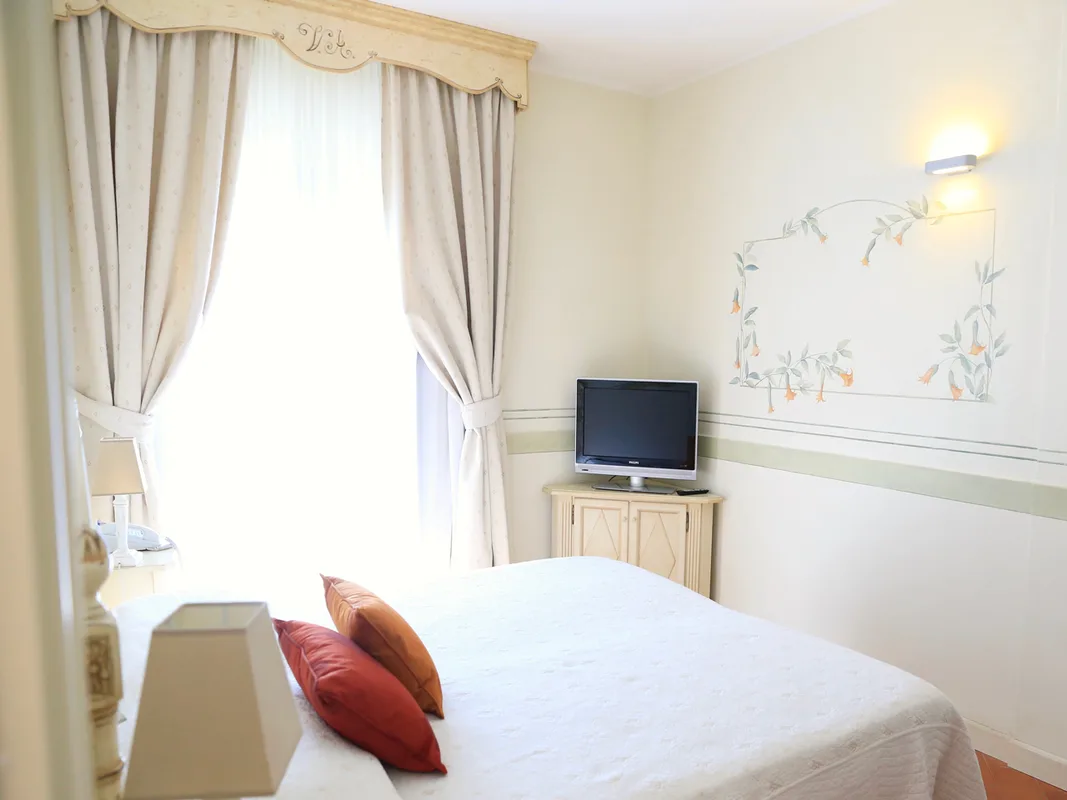 Camera con letto matrimoniale, tende beige, TV e decorazione floreale a parete
