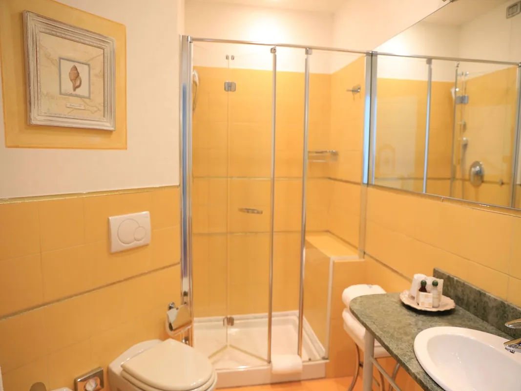 Bagno con doccia in vetro, piastrelle gialle, WC e lavabo con specchio