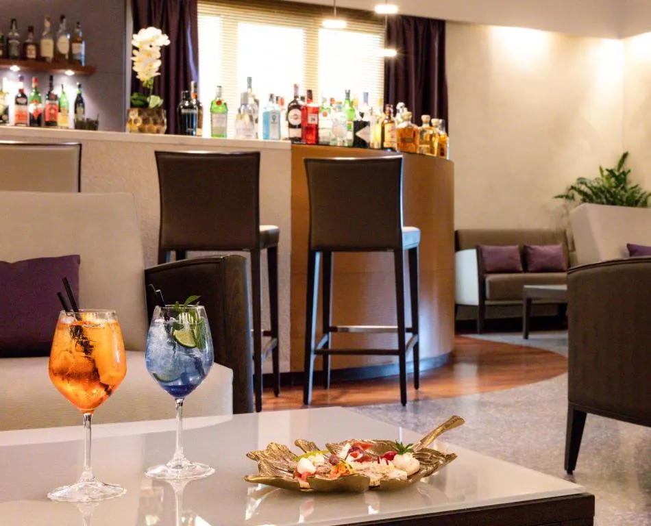 Bar interno con cocktail colorati, sgabelli e bottiglie sullo sfondo
