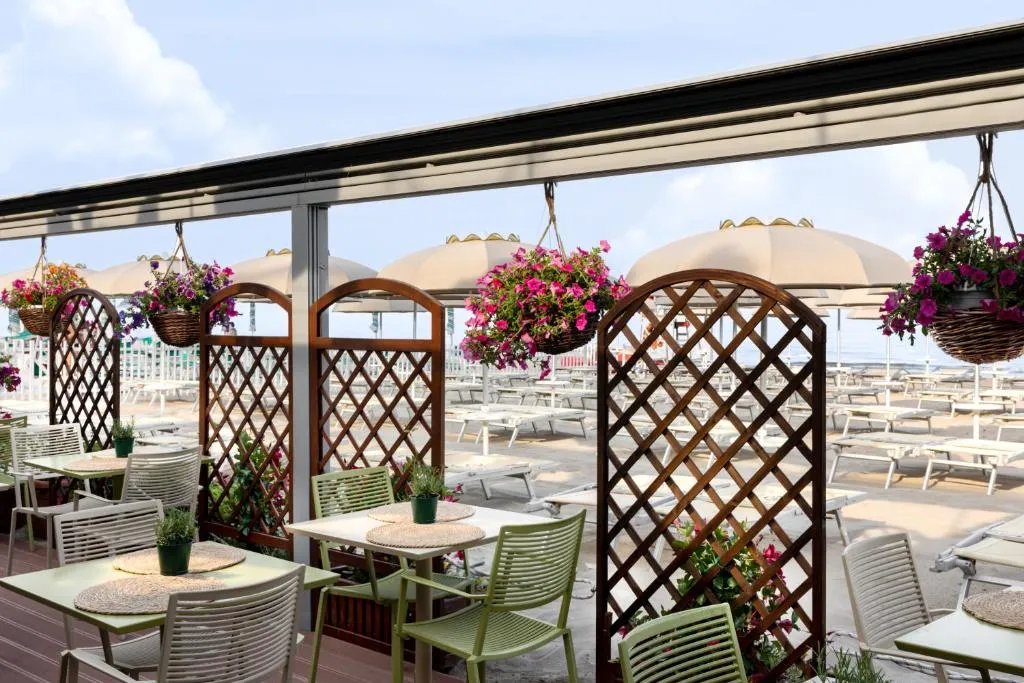 Terrazza esterna con tavoli, fiori colorati e vista sulla spiaggia attrezzata