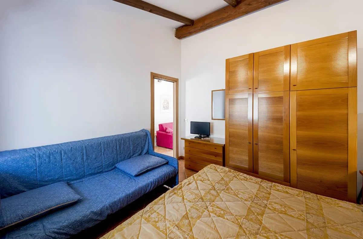 Camera con letto matrimoniale, divano blu e ampio armadio in legno