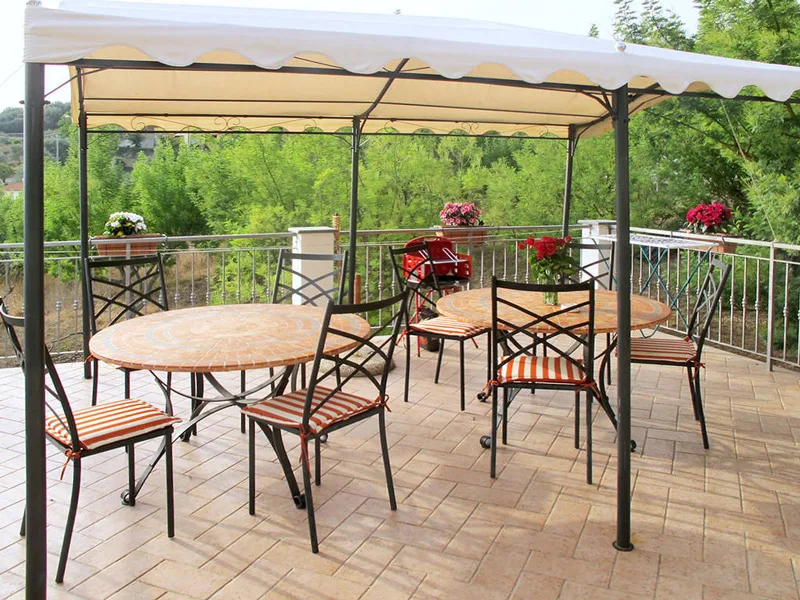Terrazza esterna con gazebo bianco, tavoli rotondi e sedie affacciata sul verde