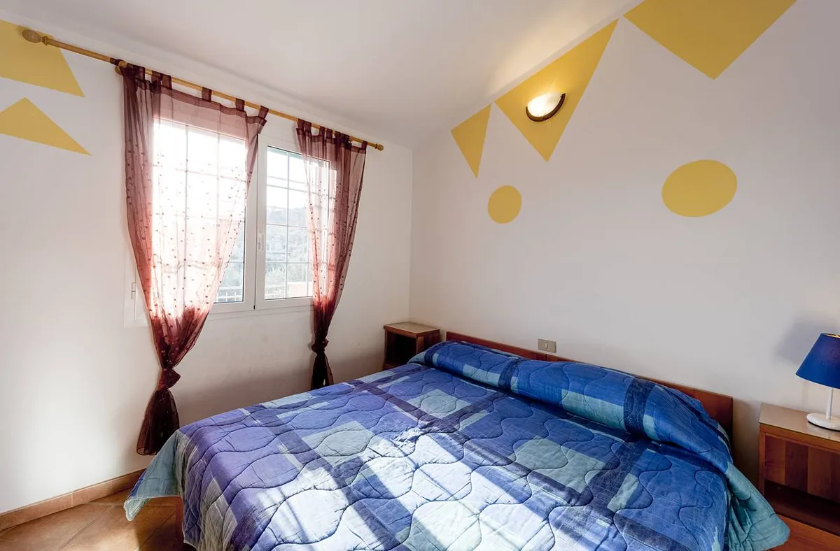 Camera da letto con letto matrimoniale blu, pareti decorate e finestra con tende