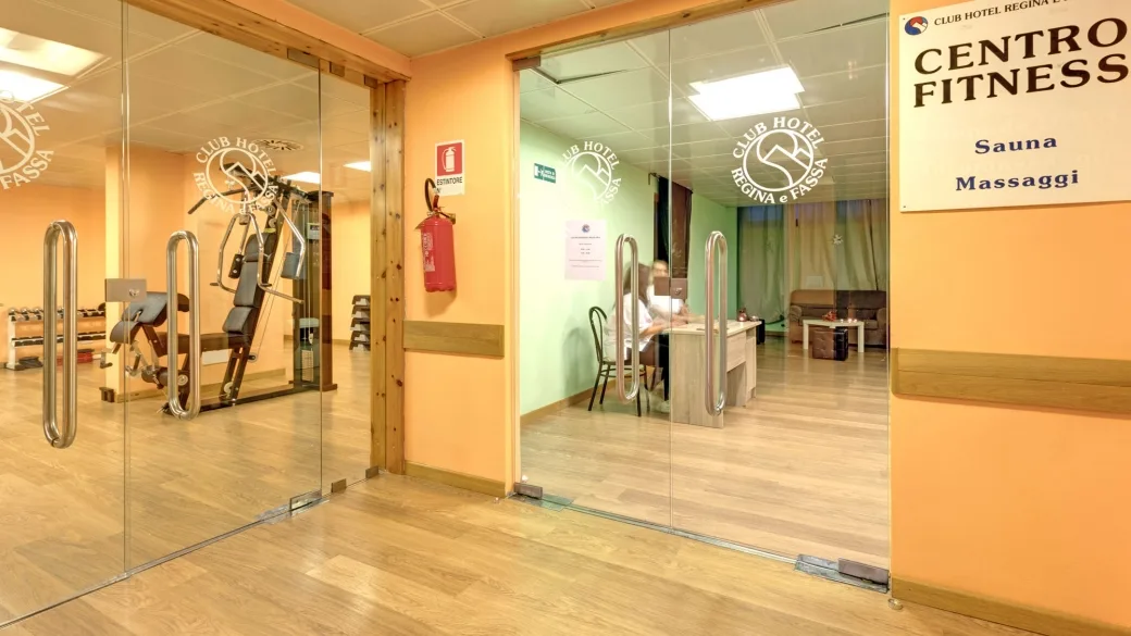 Ingresso al centro fitness con sauna e massaggi, attrezzi da palestra visibili attraverso pareti vetrate