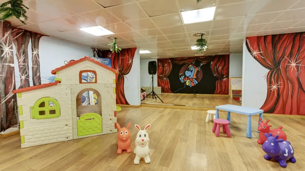Sala giochi per bambini con casetta, giochi gonfiabili e palco decorato con tende rosse